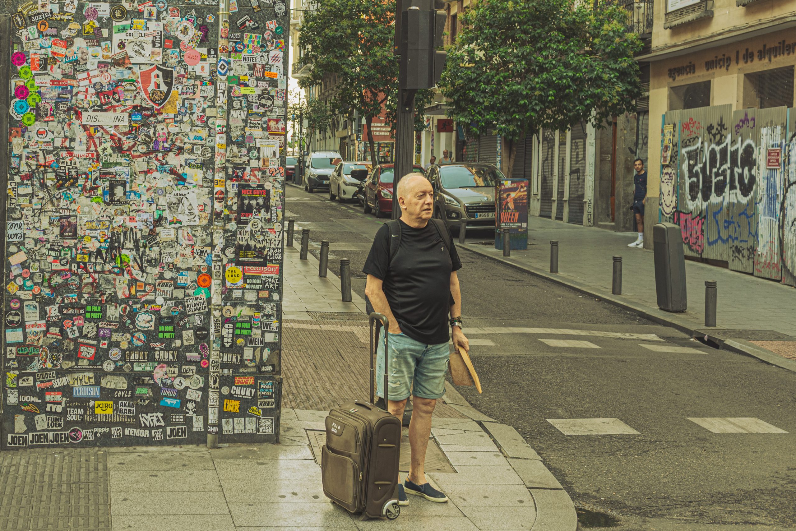 Hombre con maleta frente a un muro lleno de pegatinas en Chueca, Madrid