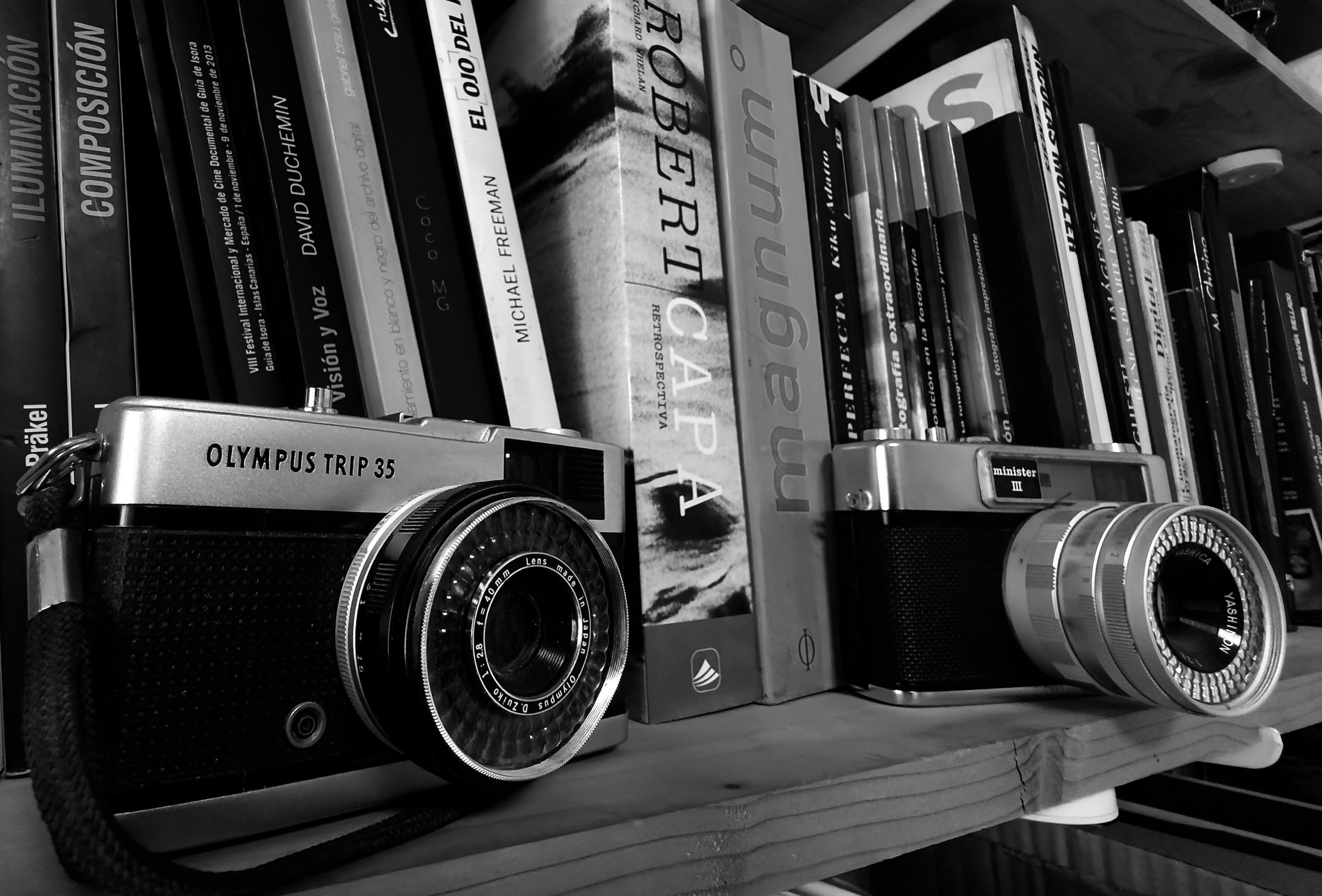 Cámaras analógicas Olympus Trip 35 y Minister III sobre estantería con libros de fotografía